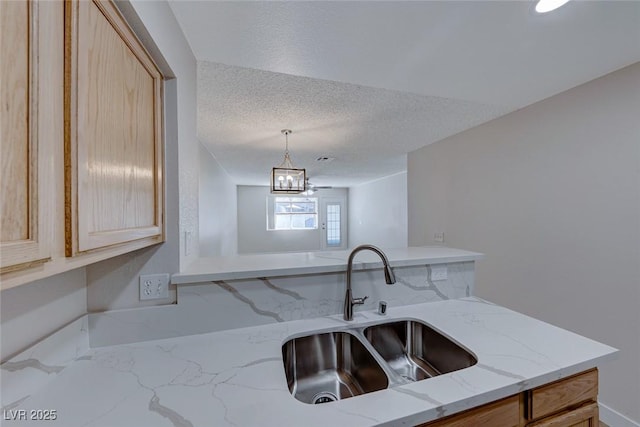 kitchen with pendant lighting, a sink, a textured ceiling, and light stone countertops