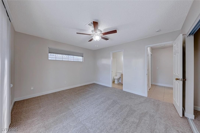 unfurnished bedroom featuring light carpet, baseboards, ceiling fan, ensuite bathroom, and a textured ceiling