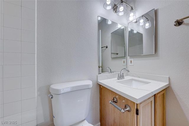 bathroom with toilet, a textured wall, and vanity