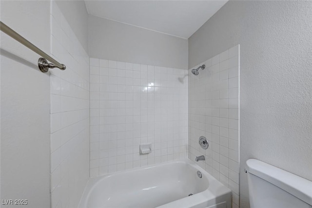 bathroom featuring toilet, washtub / shower combination, and a textured wall