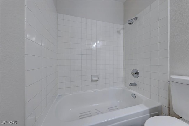 bathroom featuring a textured wall, shower / bathing tub combination, and toilet