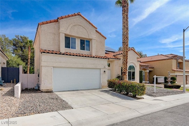 mediterranean / spanish house with an attached garage, concrete driveway, a tiled roof, roof mounted solar panels, and stucco siding