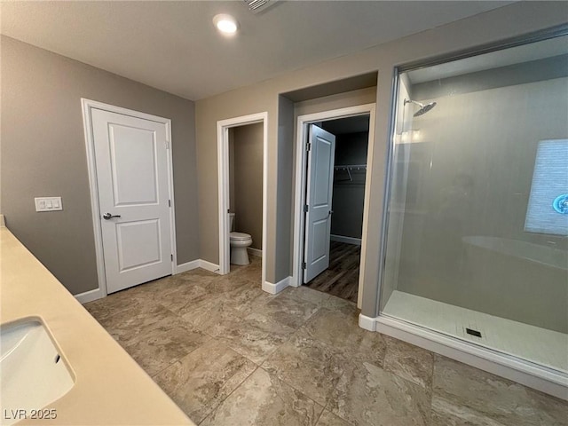 full bath featuring a walk in closet, toilet, baseboards, a sink, and a stall shower
