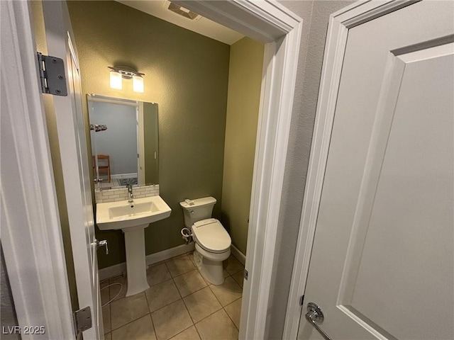 bathroom featuring tile patterned flooring, tasteful backsplash, toilet, baseboards, and a sink