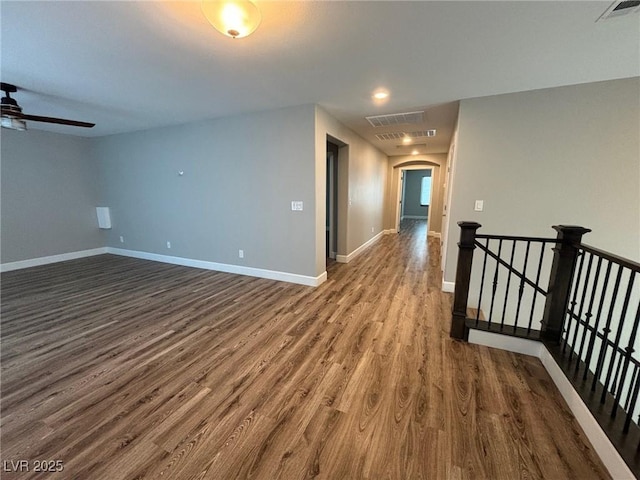 spare room featuring arched walkways, dark wood-style floors, baseboards, and visible vents