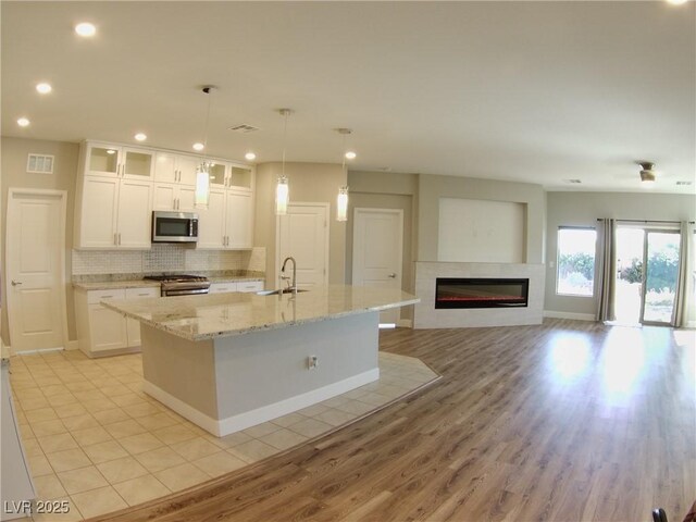 kitchen with a sink, appliances with stainless steel finishes, a center island with sink, visible vents, and white cabinets