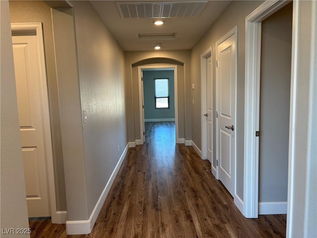 hallway featuring baseboards, visible vents, arched walkways, and dark wood-style floors