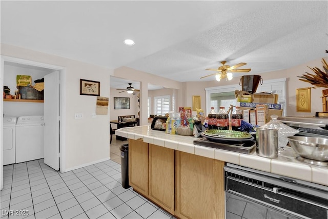 kitchen featuring a textured ceiling, dishwashing machine, light tile patterned flooring, separate washer and dryer, and tile counters