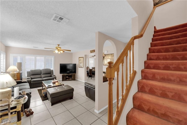 living room featuring light tile patterned floors, visible vents, a ceiling fan, stairs, and a textured ceiling