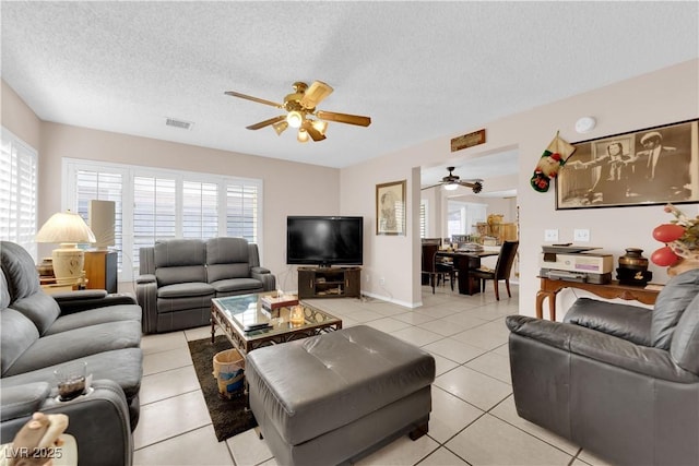 living room with light tile patterned floors, a textured ceiling, visible vents, and a ceiling fan