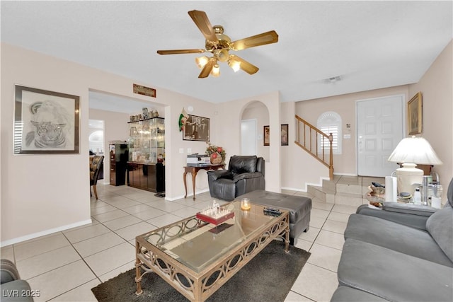 living area with arched walkways, a ceiling fan, light tile patterned flooring, baseboards, and stairs