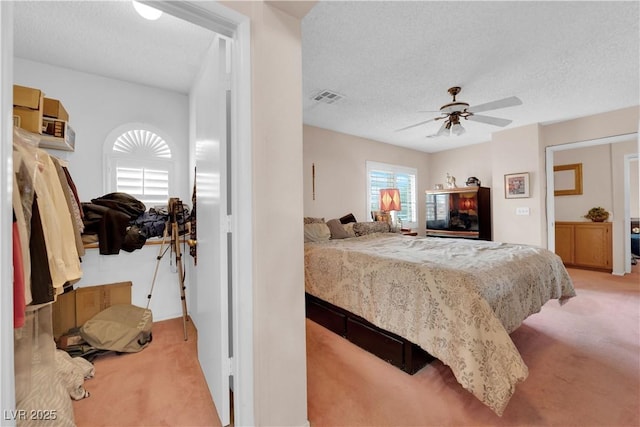 bedroom with a ceiling fan, visible vents, a textured ceiling, and light colored carpet