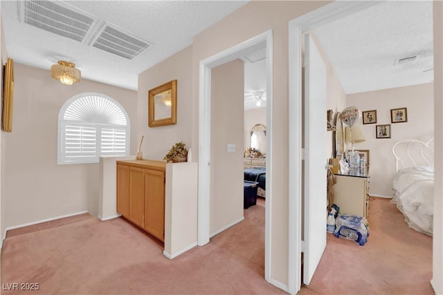 corridor with a textured ceiling, baseboards, visible vents, and light colored carpet