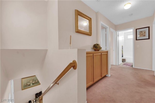 corridor featuring light carpet, a textured ceiling, and an upstairs landing