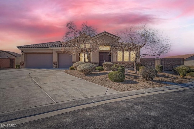 view of front of property featuring concrete driveway, stone siding, a tile roof, an attached garage, and stucco siding