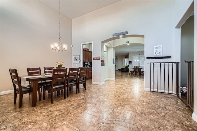 dining area with baseboards, a high ceiling, arched walkways, and a notable chandelier