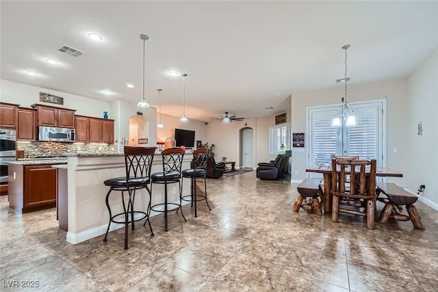 kitchen with arched walkways, brown cabinets, stainless steel appliances, visible vents, and a kitchen bar