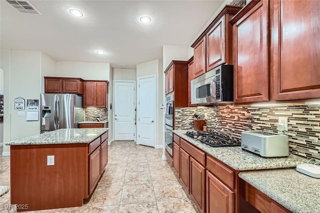 kitchen featuring stainless steel appliances, a center island, visible vents, and light stone countertops