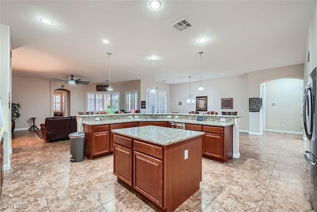 kitchen featuring arched walkways, a sink, visible vents, a center island, and brown cabinets