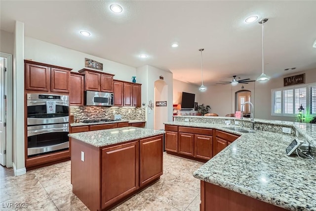 kitchen with arched walkways, a kitchen island, a sink, appliances with stainless steel finishes, and decorative backsplash