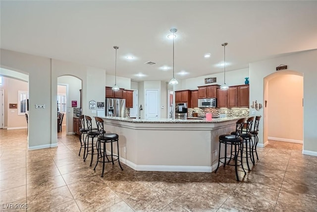 kitchen featuring tasteful backsplash, a kitchen bar, appliances with stainless steel finishes, and arched walkways