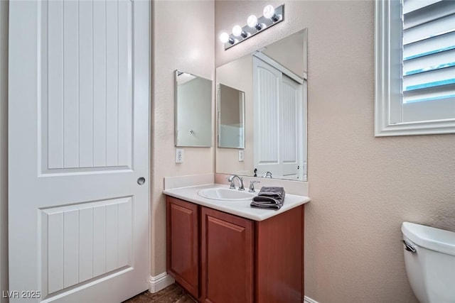 half bathroom featuring a textured wall, vanity, and toilet