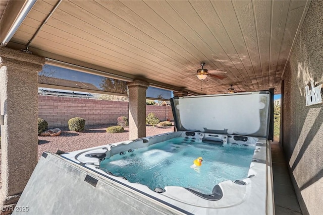 view of swimming pool with ceiling fan, fence, and a hot tub