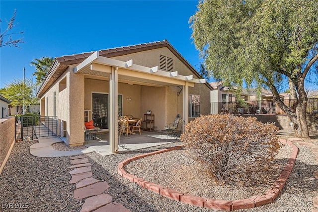 rear view of house featuring a patio area, fence, and stucco siding