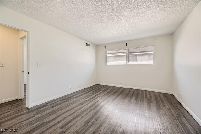 spare room featuring dark wood-type flooring, visible vents, and baseboards