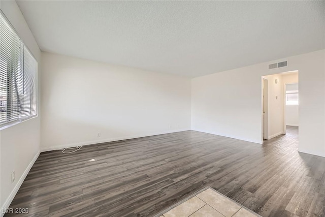 unfurnished room with visible vents, plenty of natural light, a textured ceiling, and wood finished floors