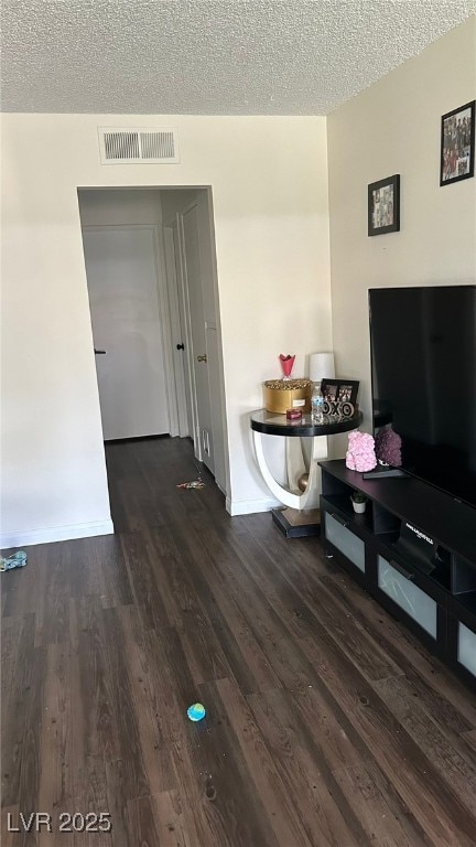 living area with a textured ceiling, wood finished floors, visible vents, and baseboards