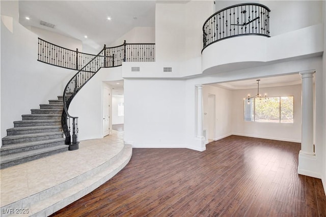 entrance foyer with dark wood-type flooring, a towering ceiling, visible vents, and ornate columns