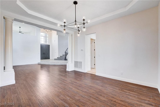 unfurnished dining area featuring ornate columns, a raised ceiling, and wood finished floors