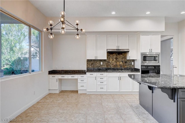 kitchen featuring dark stone counters, appliances with stainless steel finishes, a wealth of natural light, and under cabinet range hood