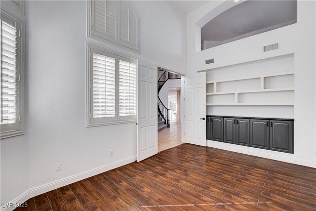 unfurnished living room featuring baseboards, visible vents, dark wood finished floors, built in features, and stairs