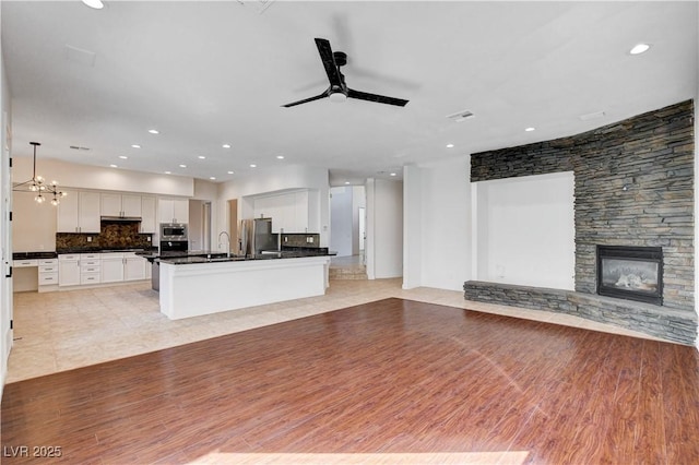 kitchen featuring stainless steel appliances, dark countertops, a ceiling fan, open floor plan, and a stone fireplace