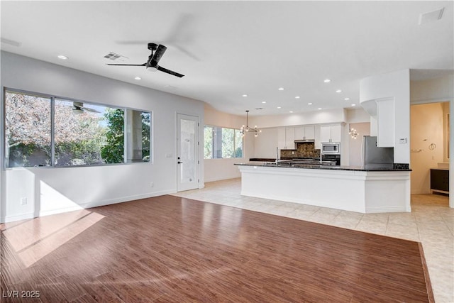 kitchen featuring white cabinets, decorative backsplash, dark countertops, appliances with stainless steel finishes, and ceiling fan with notable chandelier