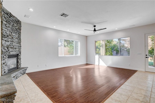 unfurnished living room with a stone fireplace, wood finished floors, a ceiling fan, visible vents, and baseboards