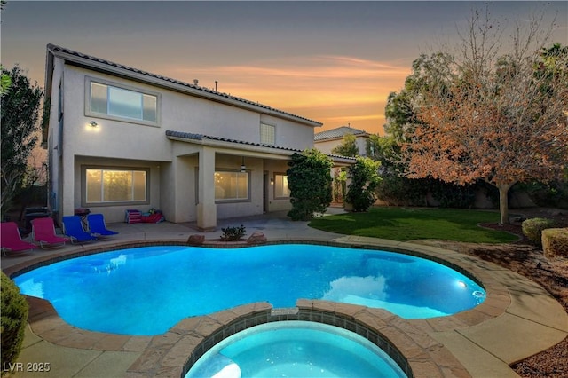 pool at dusk featuring a yard, a pool with connected hot tub, and a patio