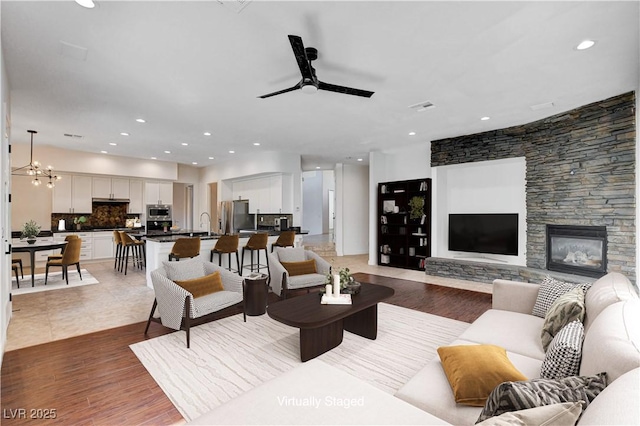 living room with ceiling fan with notable chandelier, light wood finished floors, a fireplace, and recessed lighting