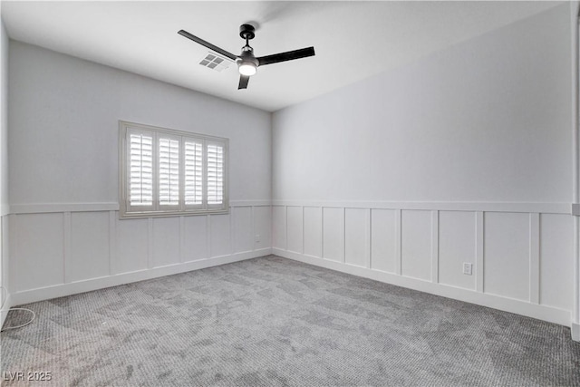 spare room with ceiling fan, a decorative wall, carpet floors, visible vents, and wainscoting