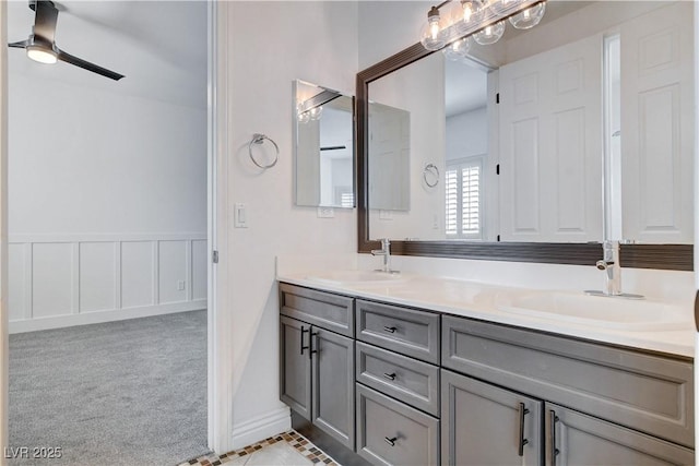 bathroom with a wainscoted wall, double vanity, ceiling fan, and a sink