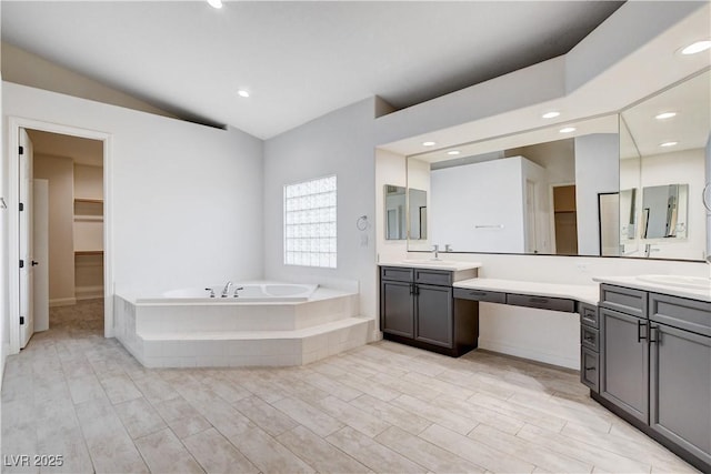 bathroom featuring lofted ceiling, vanity, a garden tub, and a walk in closet