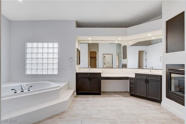 full bathroom with a garden tub, recessed lighting, a glass covered fireplace, and vanity