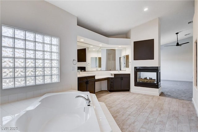 bathroom featuring lofted ceiling, ceiling fan, a garden tub, vanity, and a multi sided fireplace