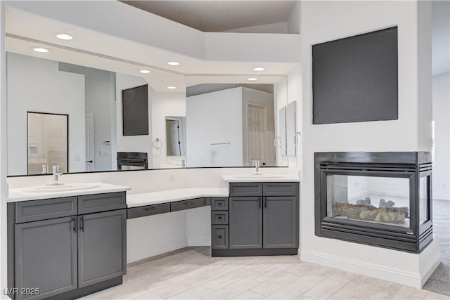 full bathroom featuring wood finished floors, a multi sided fireplace, vanity, and recessed lighting