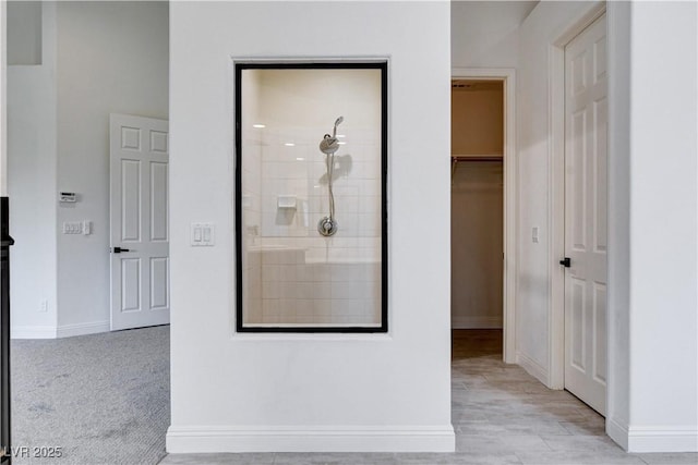 full bath featuring a tile shower, a walk in closet, and baseboards