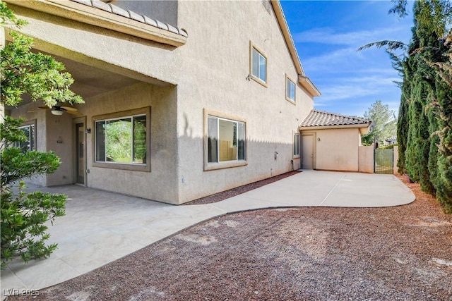 view of side of property with stucco siding, a tile roof, a ceiling fan, and a patio