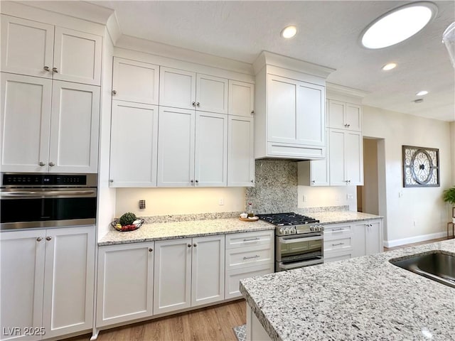 kitchen with light stone counters, recessed lighting, white cabinetry, appliances with stainless steel finishes, and light wood-type flooring