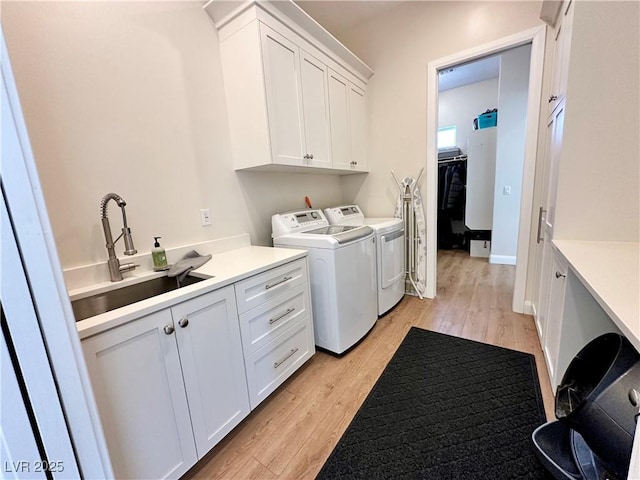 washroom with a sink, baseboards, light wood-type flooring, cabinet space, and washer and clothes dryer